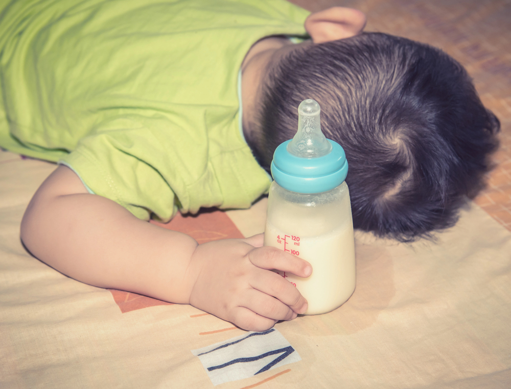 baba hason fekszik, kezében tejesüveg baba hason fekszik, kezében tejesüveg